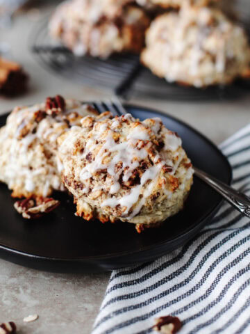 Cinnamon Bun Scones drizzled with icing on a black plate.