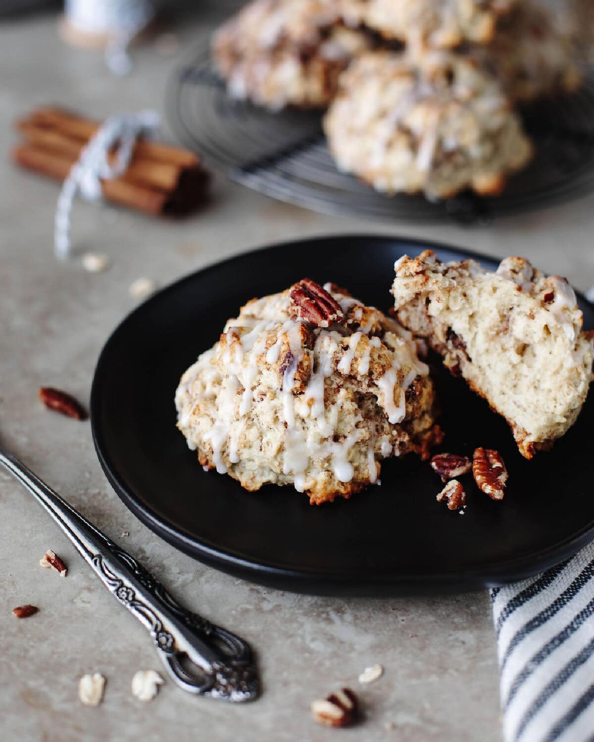 two cinnamon pecan scones with a glaze on a black plate.