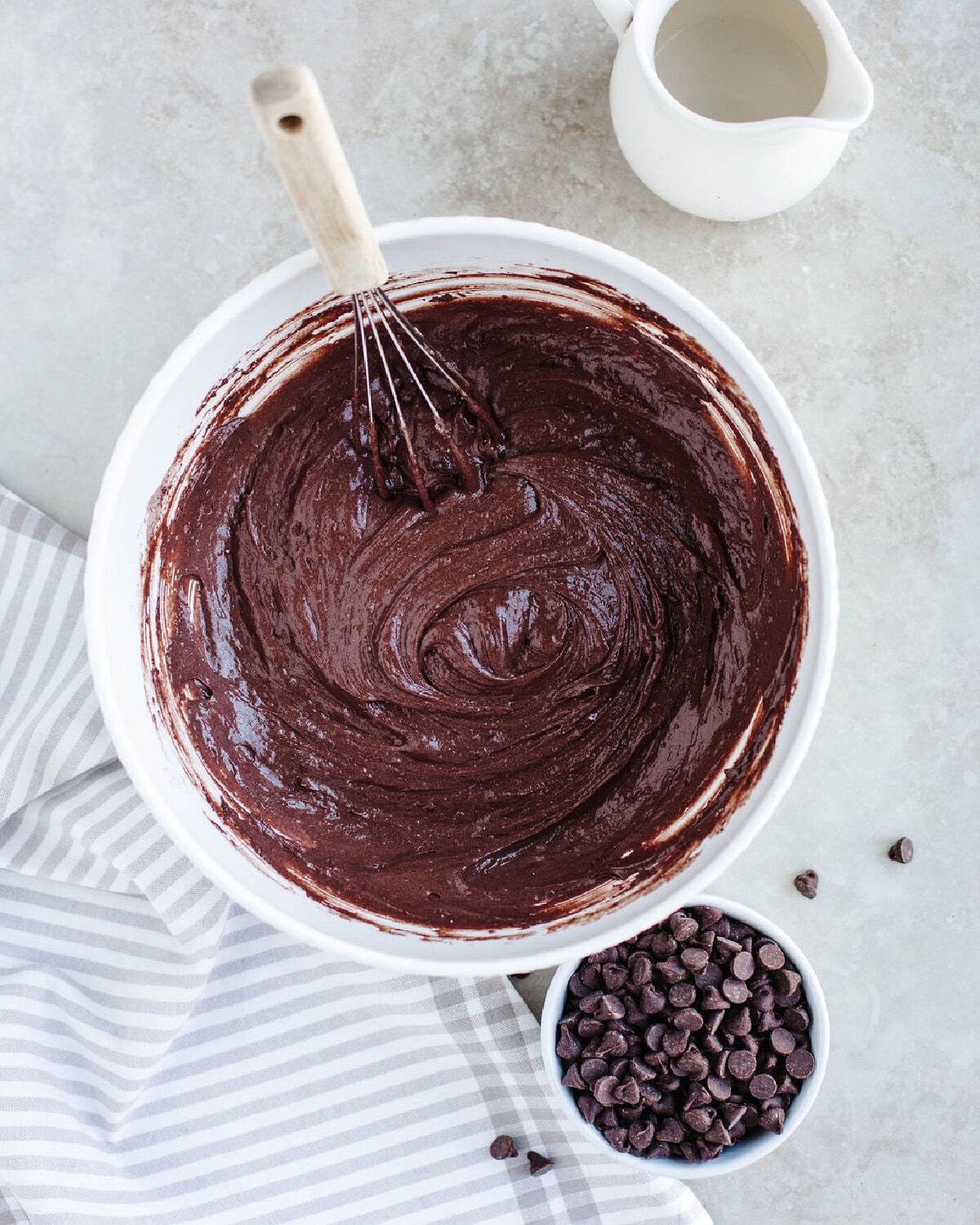 chocolate dump cake batter in a white mixing bowl with chocolate chips getting added in.