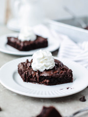 an ooey gooey dump cake piece served on a white plate with whipped cream.