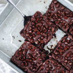 a spatula scooping out a piece of chocolate dump cake with melted chocolate chips on top.
