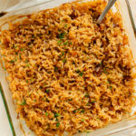 a serving spoon scooping French Onion rice out of an 8x8 baking dish.