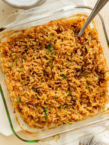 a serving spoon scooping French Onion rice out of an 8x8 baking dish.