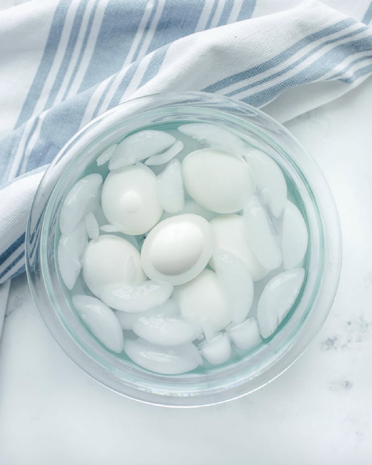 hard boiled eggs cooling in an ice bath in a glass mixing bowl.