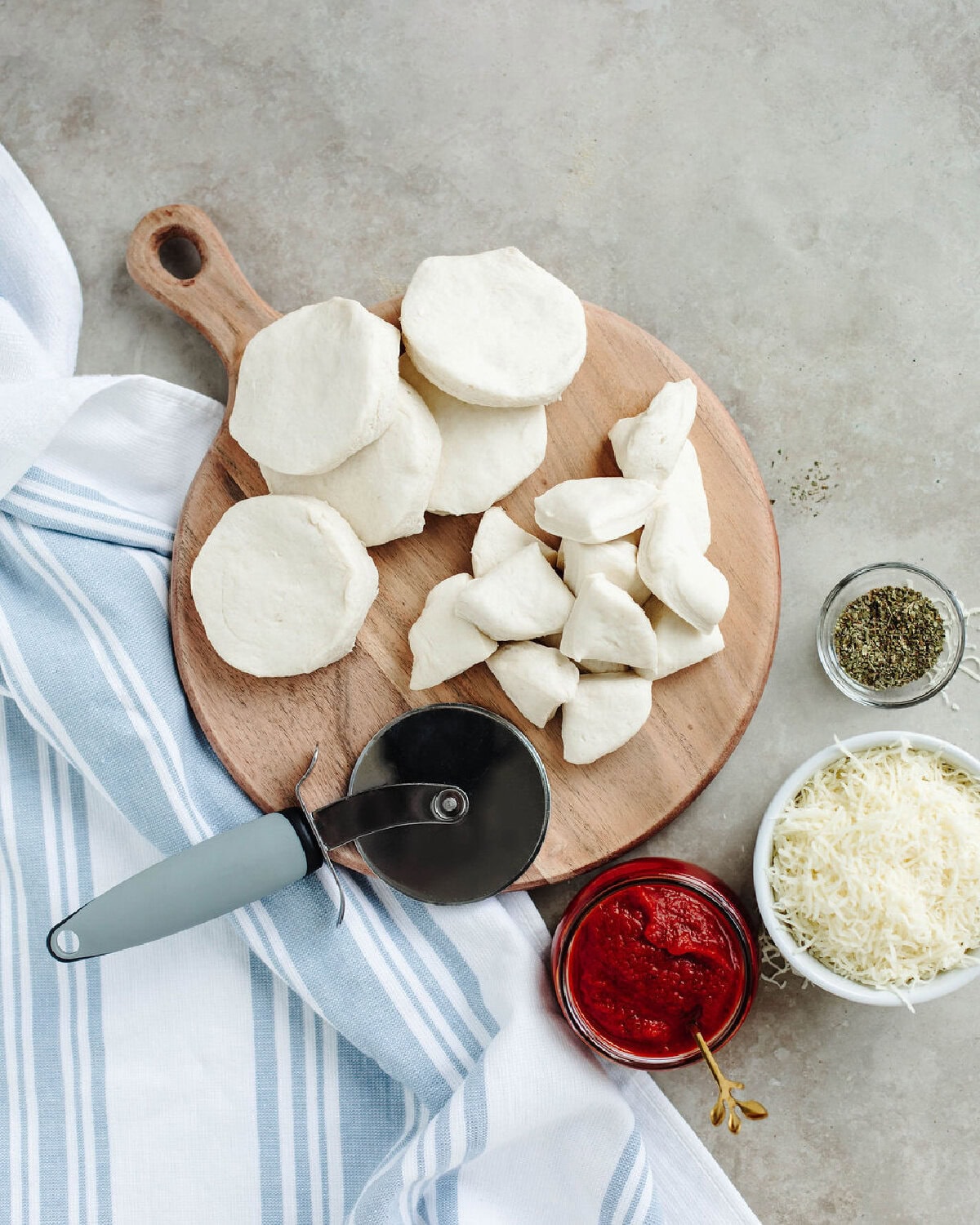 biscuits being quartered with a pizza slicer on a wood cutting board.
