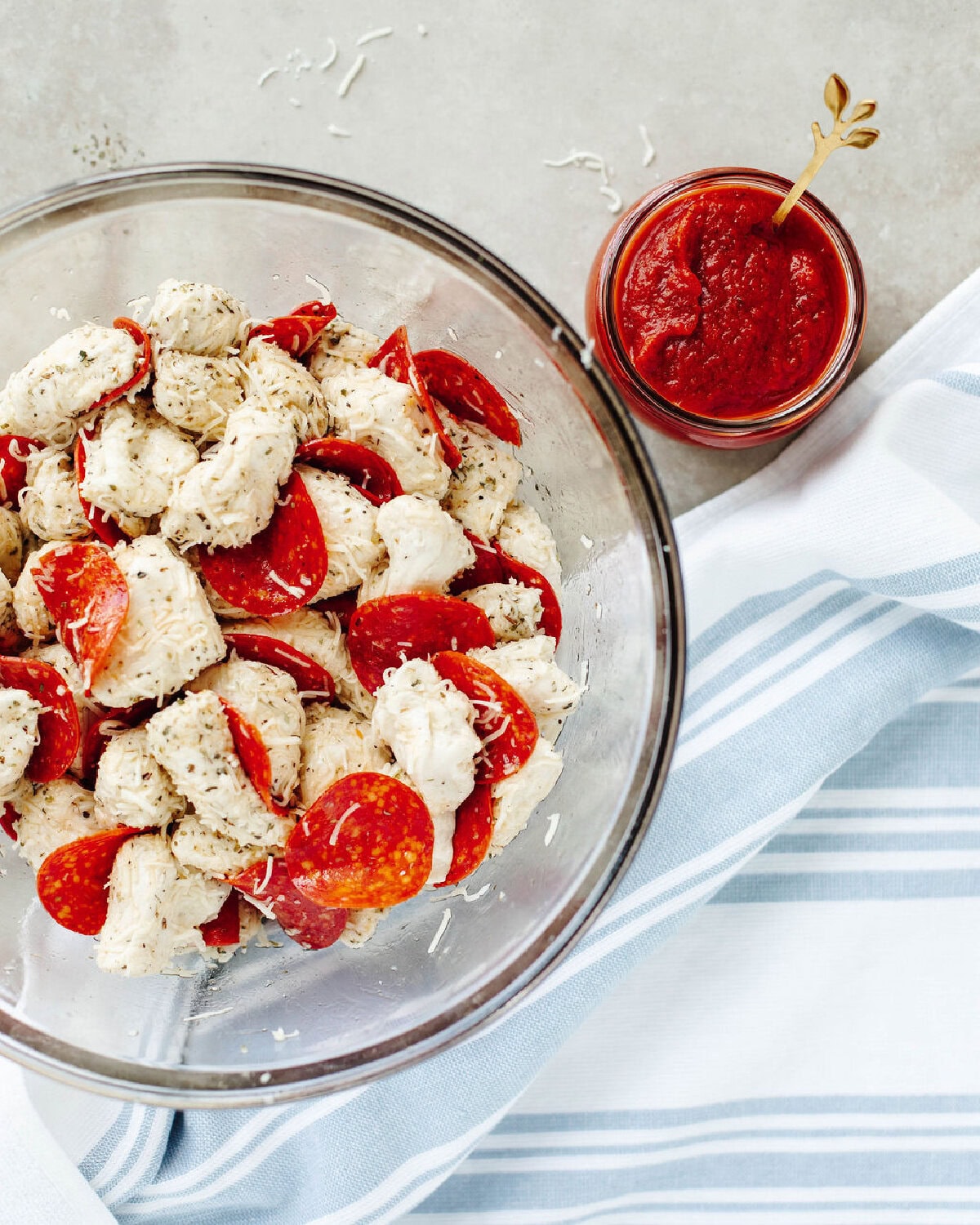 quartered biscuit dough combined with Italian seasoning, cheese, olive oil, and pepperoni in a glass mixing bowl.