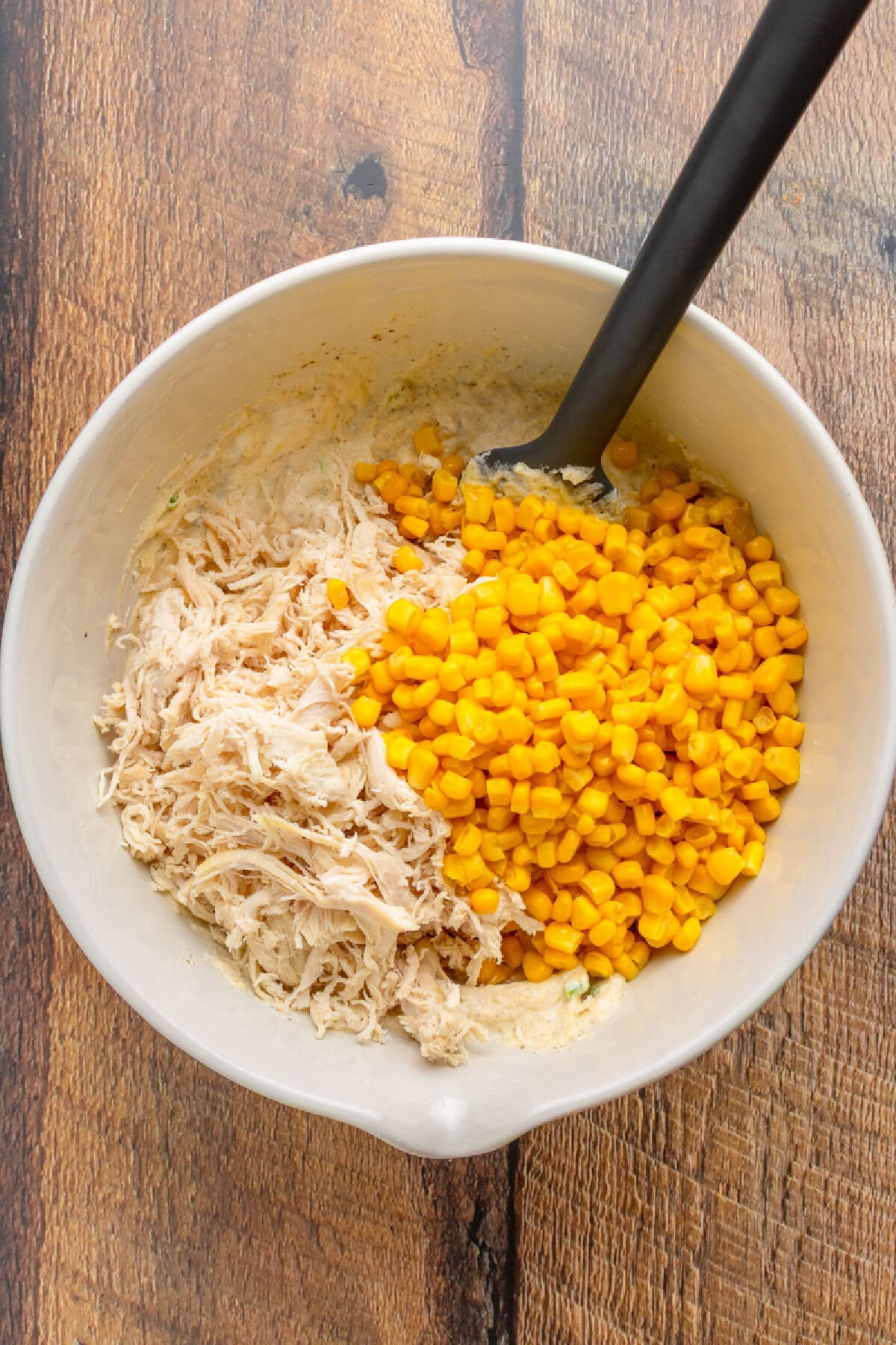 Mixing cooked chicken with creamy casserole sauce in a large bowl.