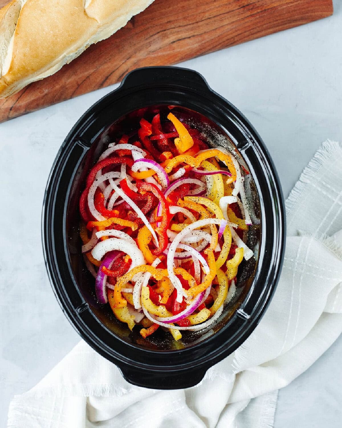 sliced peppers and onions seasoned with salt and pepper in a slow cooker.