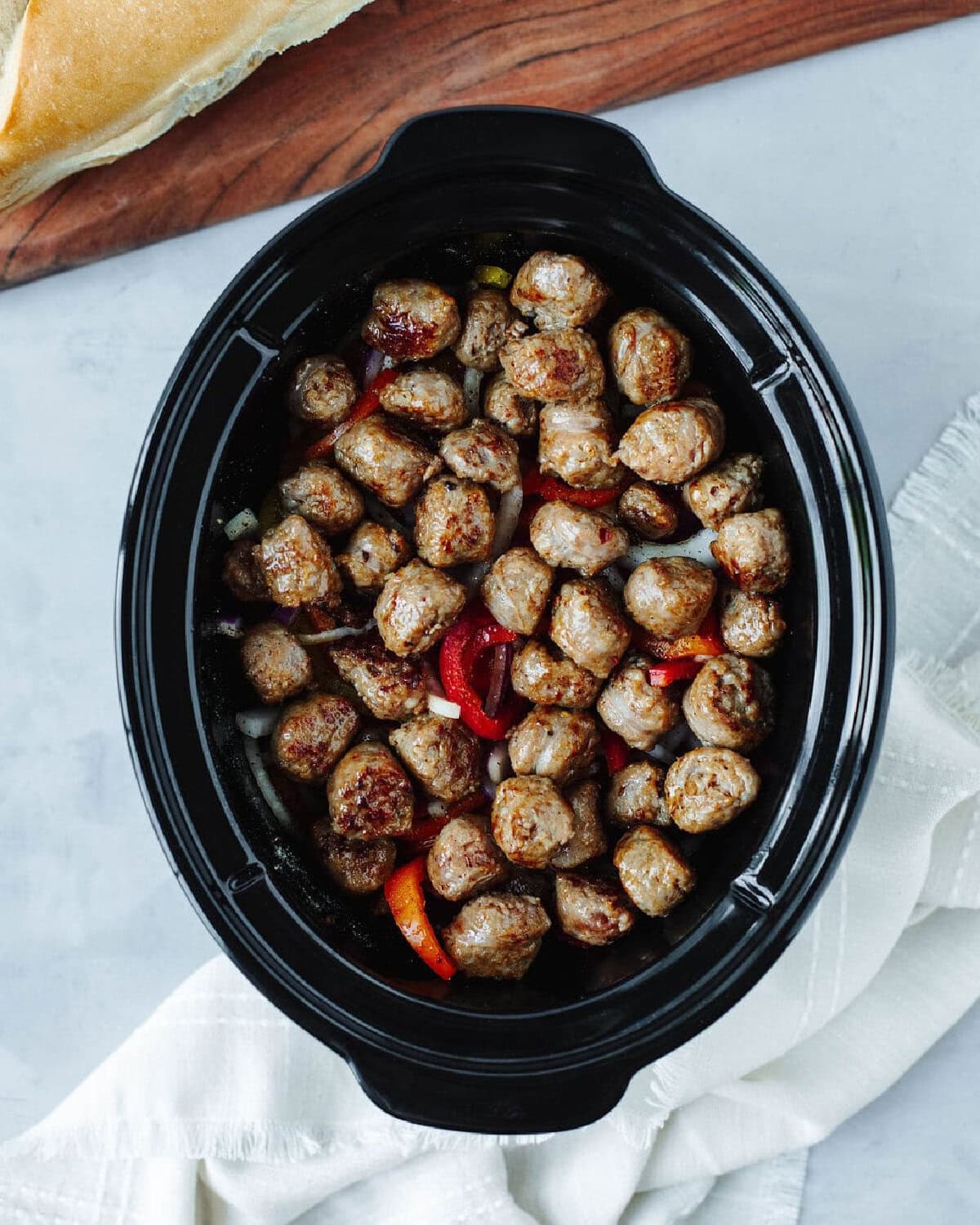 cooked sausage, peppers, and onions in a black crockpot liner.