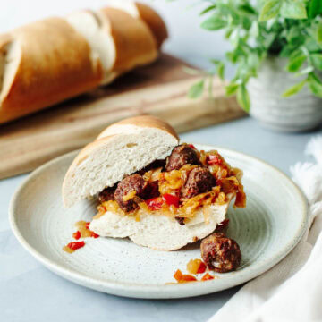 slow cooker sausage, peppers, and onions on a hoagie roll served on a plate.