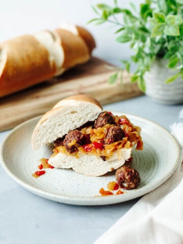 slow cooker sausage, peppers, and onions on a hoagie roll served on a plate.