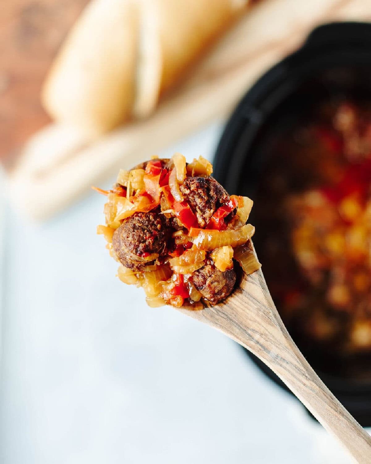 a wood spatula scooping sausage and peppers.