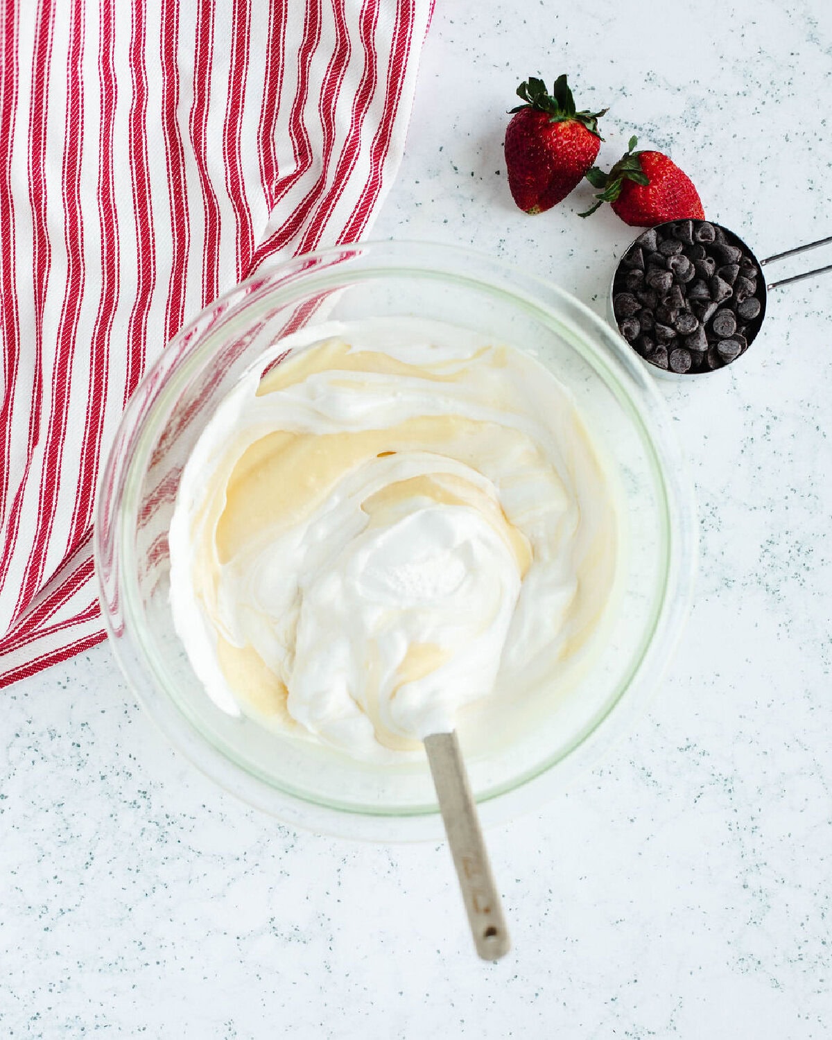 Cool whip stirred into instant vanilla pudding in a glass mixing bowl.