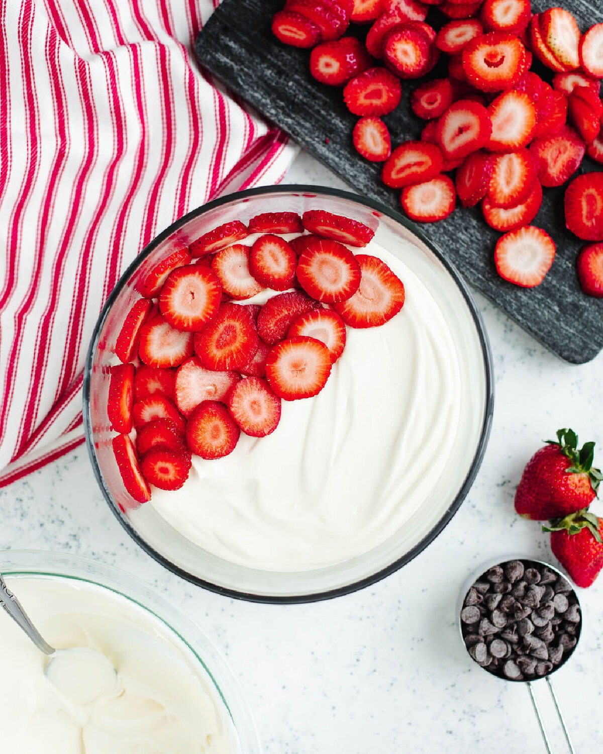 Sliced strawberries placed over a creamy pudding mixture in a glass trifle bowl.