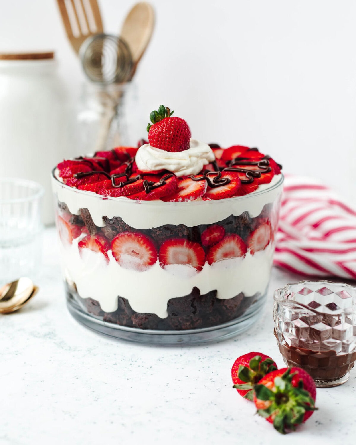 A layered strawberry brownie trifle in a glass bowl ready to serve in small glass parfait dishes.