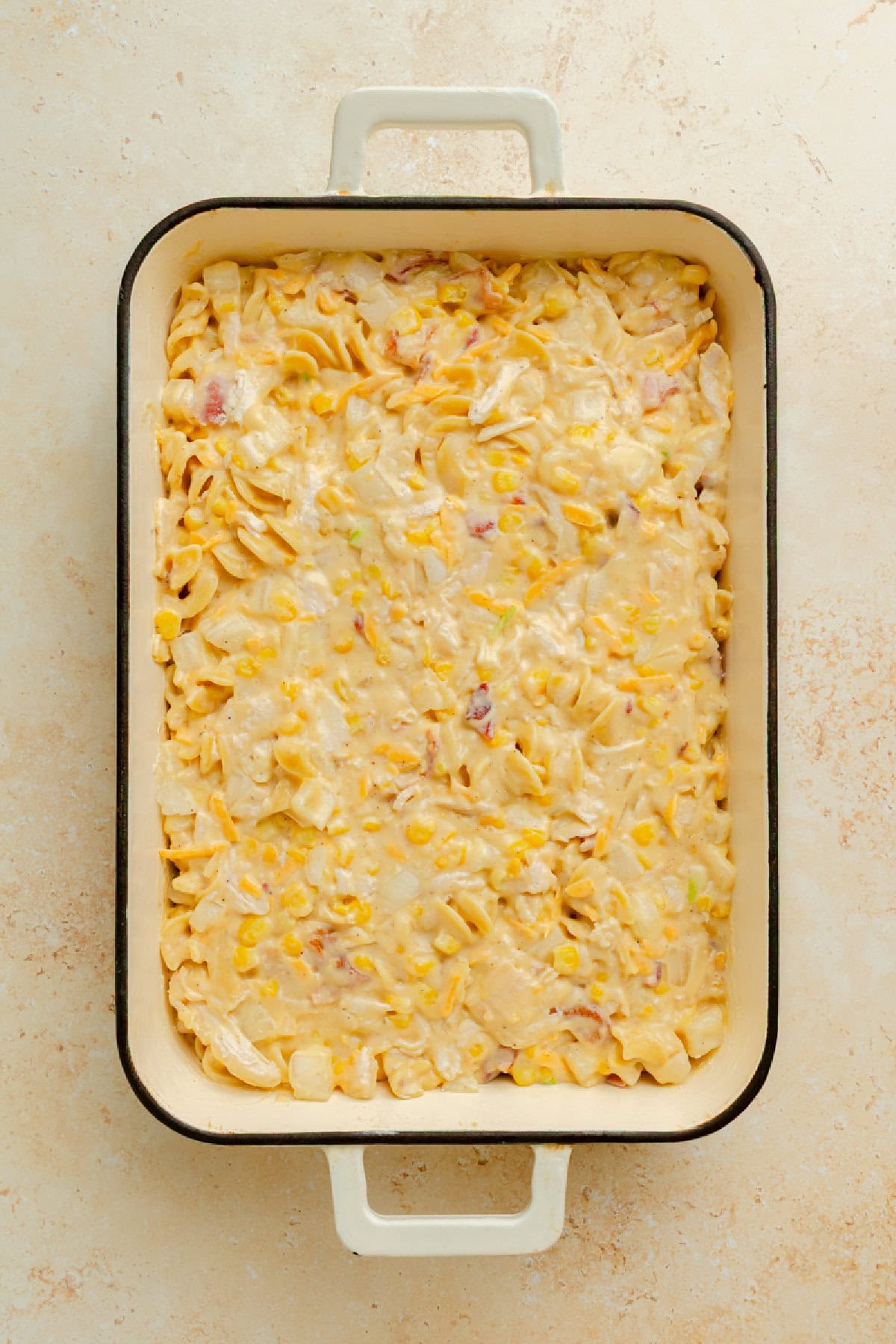 Chicken, corn, bacon, cheese, pasta, and seasonings combined in a creamy sauce and spread into a baking dish.