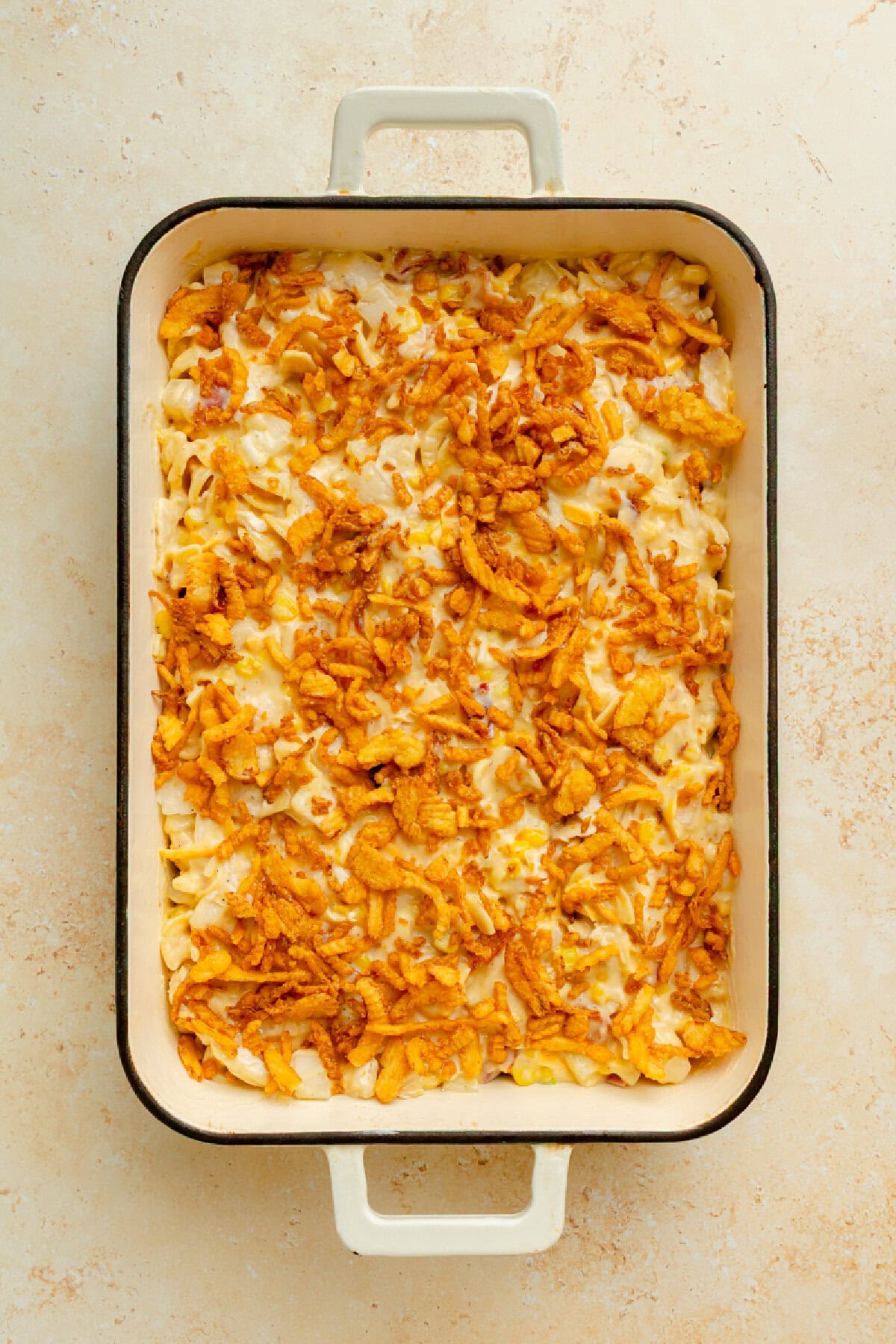 French fried onions sprinkled on top of chicken casserole in a pan ready for the oven.