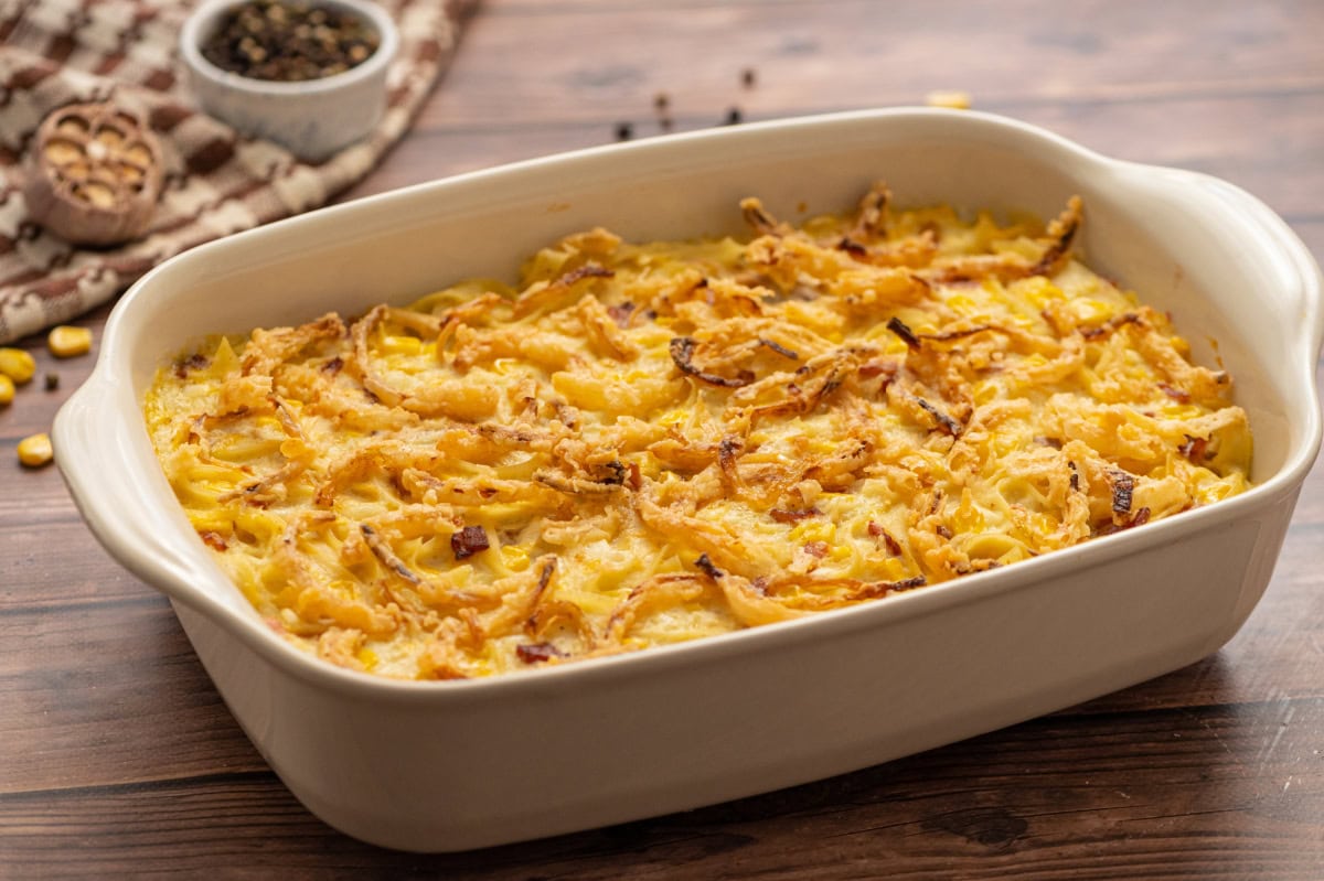 Baked chicken casserole with a fried onion topping in a cream colored baking pan.