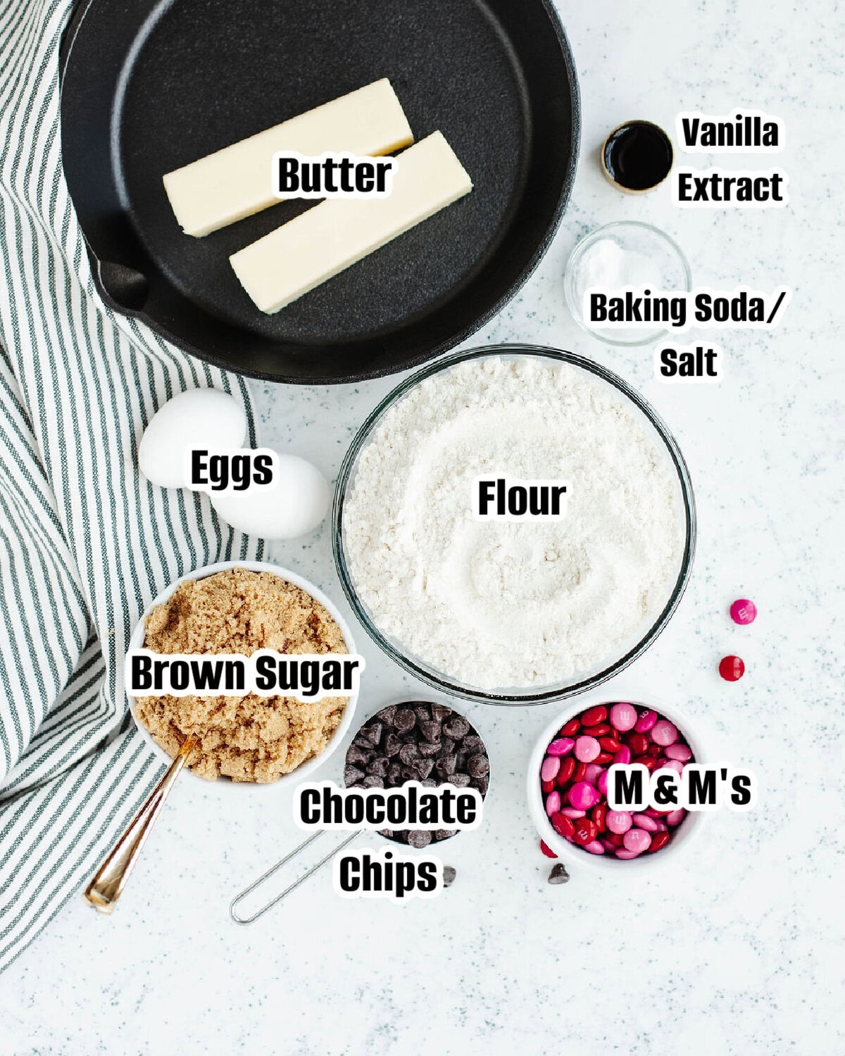 Ingredients for a chocolate chip skillet cookie including butter, brown sugar, flour, chocolate chips, and M&M's.