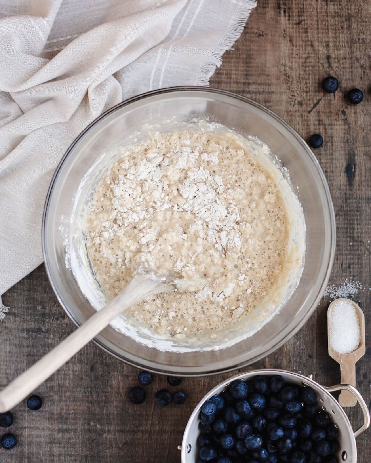 Flour, salt, and baking powder added to an egg, vanilla, milk mixture in a glass mixing bowl.