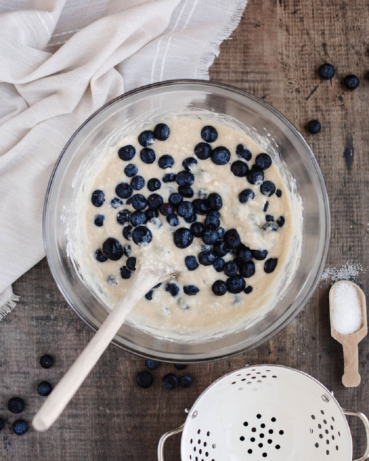 Fresh blueberries folded into bread batter in a glass mixing bowl.