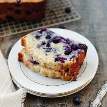 Two slices of blueberry muffin bread stacked on a white plate.