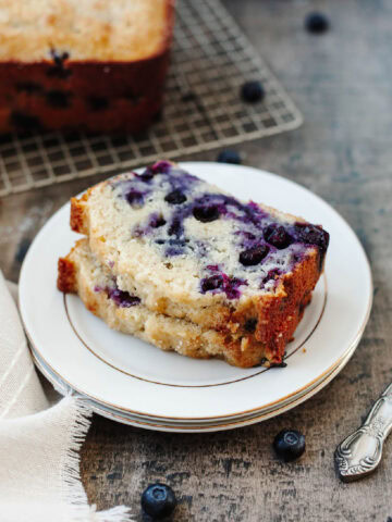 Two slices of blueberry muffin bread stacked on a white plate.