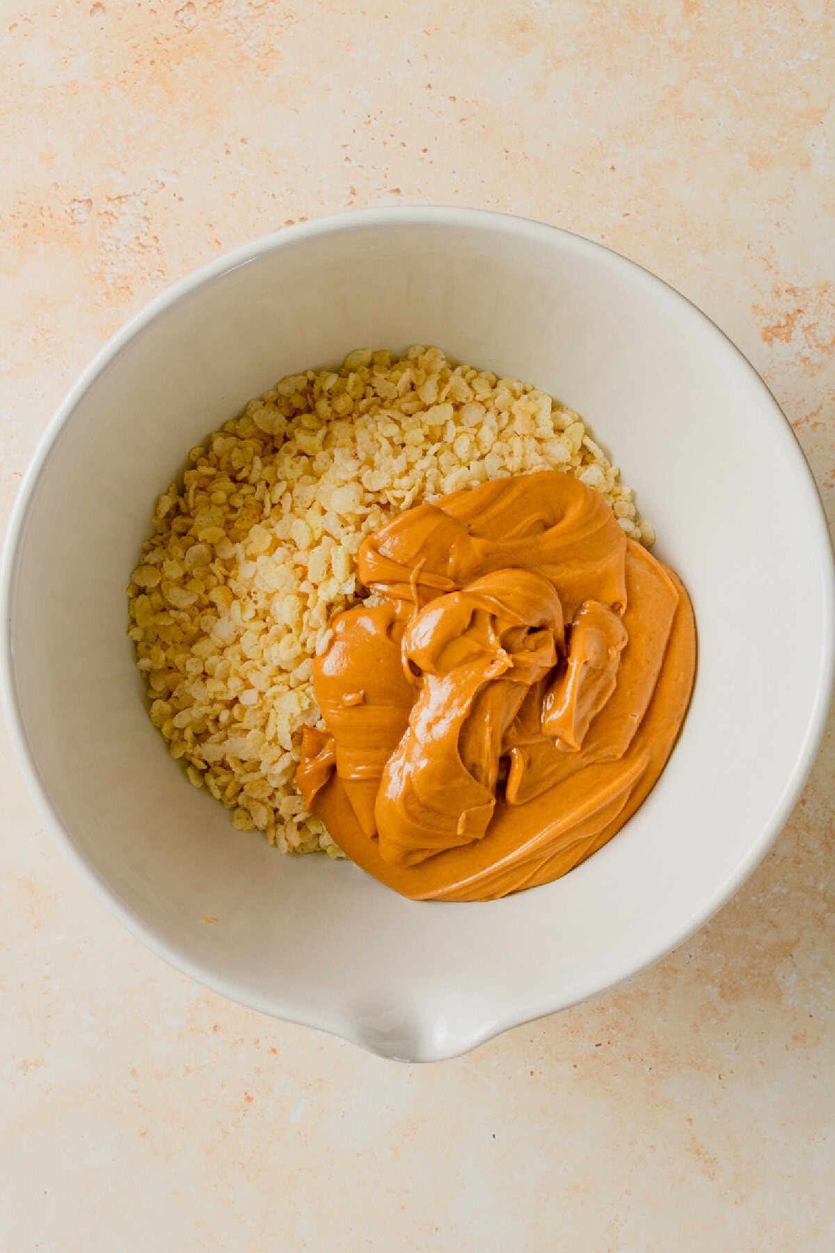 Warm peanut butter mixture poured over crispy rice cereal in a mixing bowl.