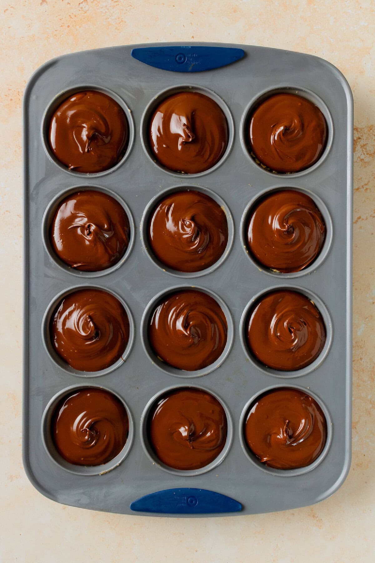 Melted chocolate being spooned over peanut butter rice krispie cups.