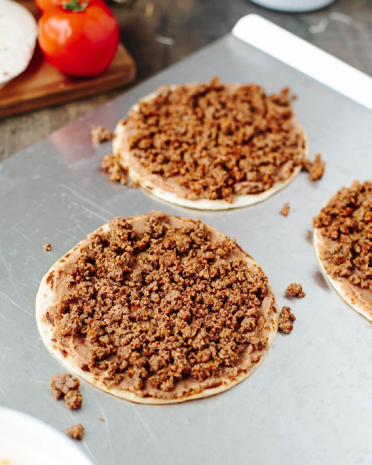 Taco seasoned ground beef over a layer of refried beans on a flour tortilla.