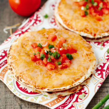 Cheesy Mexican pizzas on a serving place with diced tomatoes and green onions ready to serve.