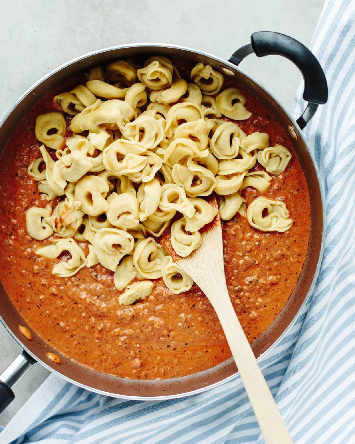 Cooked tortellini added to a spaghetti sauce mixture in a skillet.