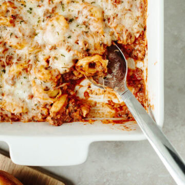 Creamy baked tortellini in a white baking pan ready to serve with a spoon.