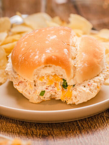 A crockpot crack chicken sandwich served on a plate with chips.