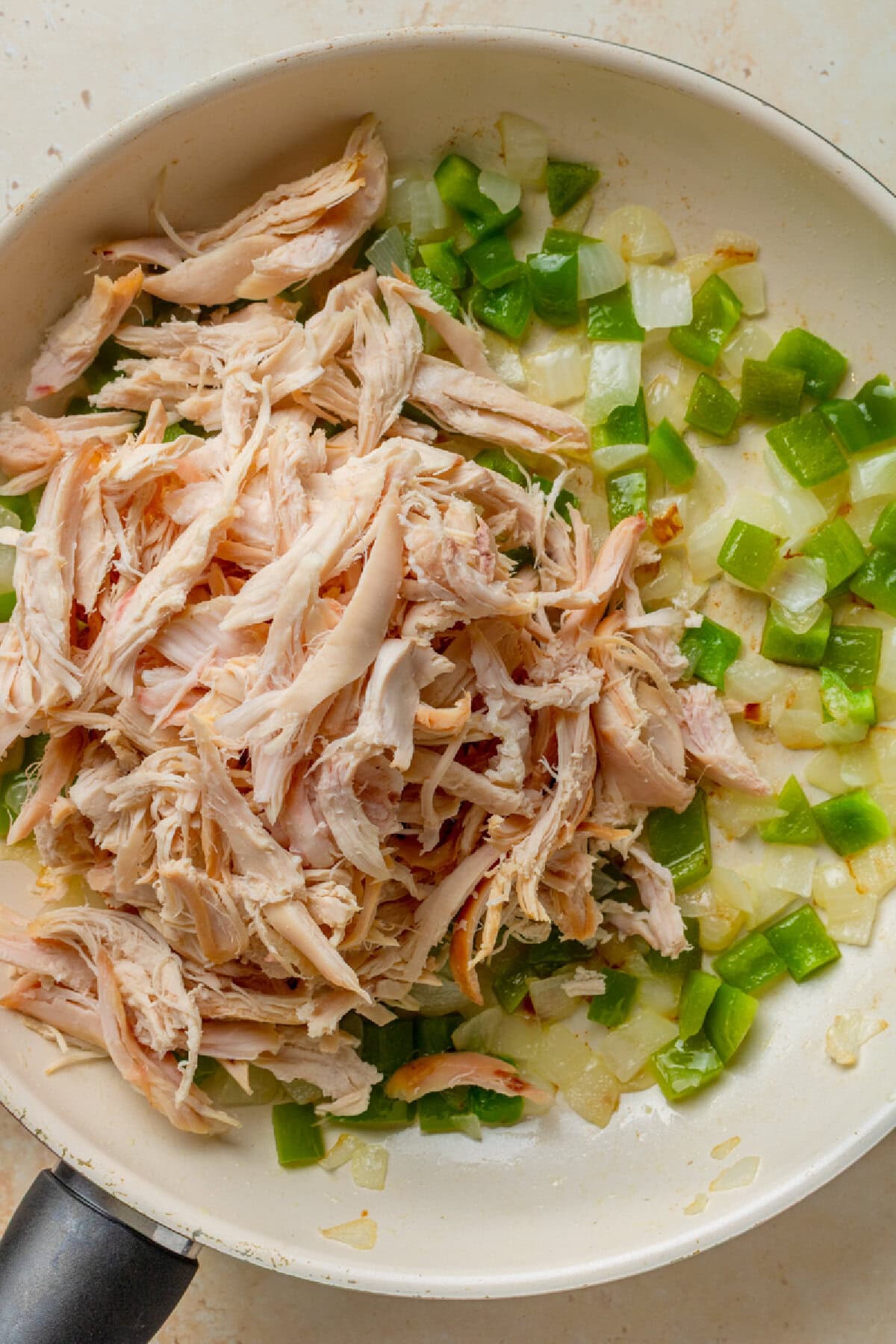 Shredded chicken added to sauteed onions and green peppers in a skillet.