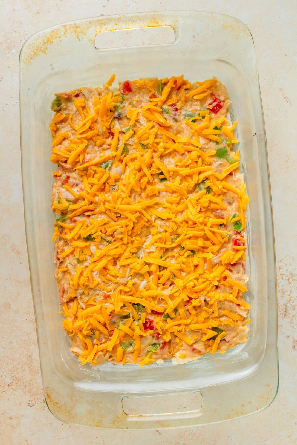Shredded cheese on top of a chicken casserole mixture in a glass 9x13 baking pan.