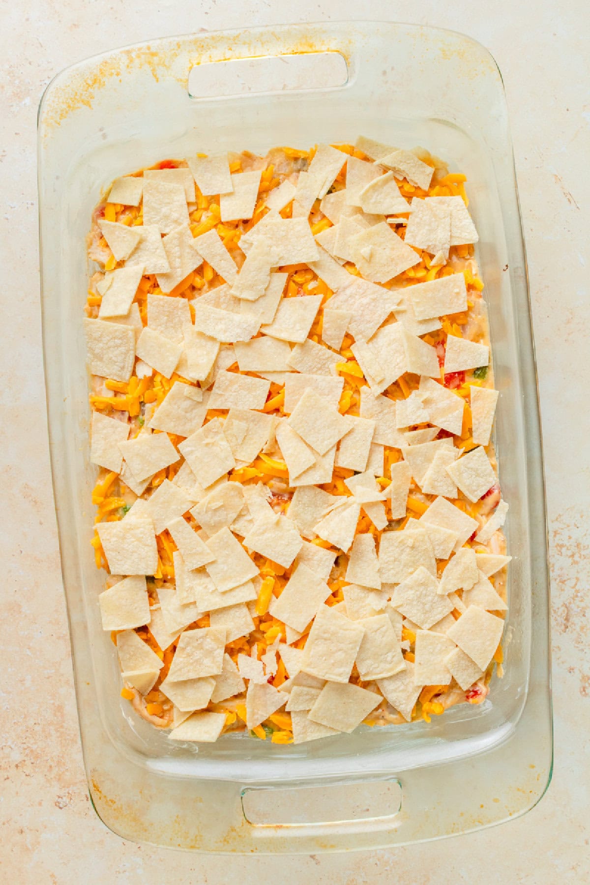 Chopped tortilla pieces on top of a chicken casserole in a 9x13 baking pan.