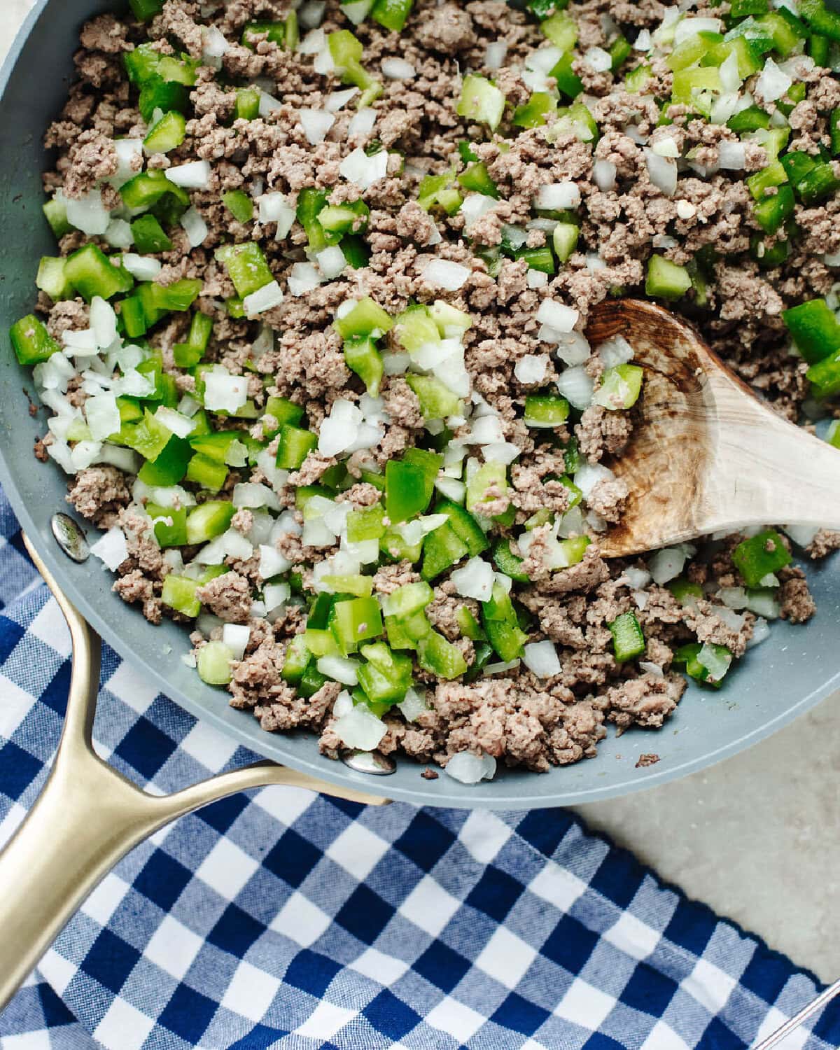 Ground beef, chopped green peppers, and onion cooking in a skillet.