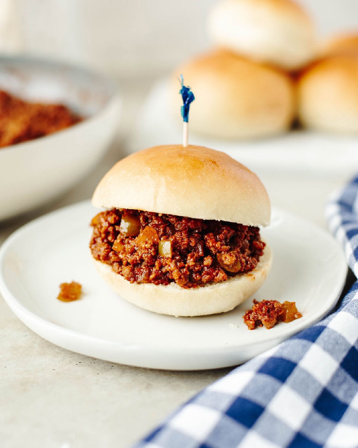 A sloppy joe sandwich on a white plate with a toothpick in the center.