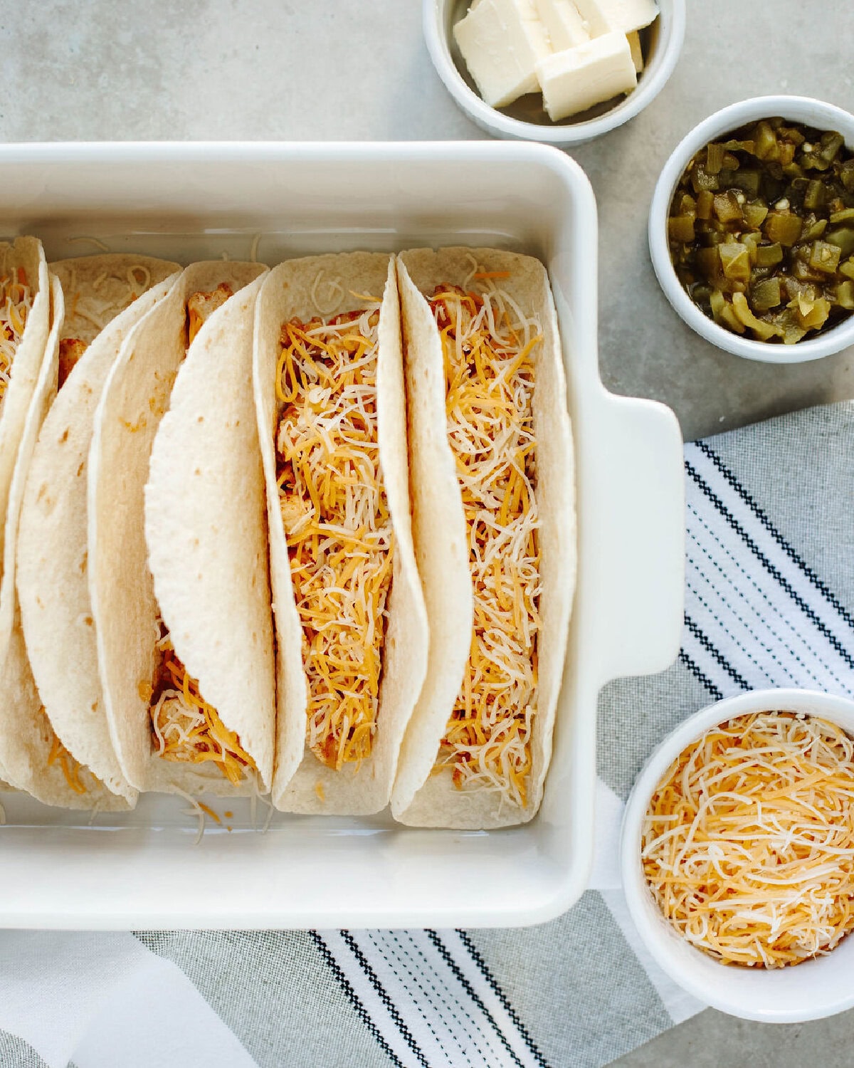 Flour tortillas filled with seasoned chicken and shredded cheese in a baking dish.