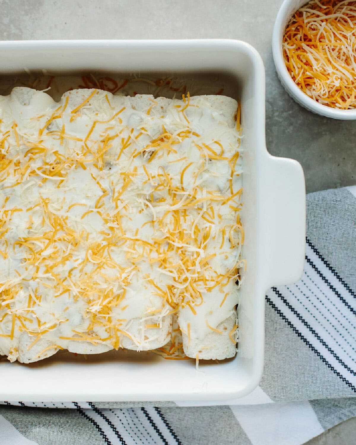Sour cream sauce poured on top of chicken filled tortillas with shredded cheese on top.