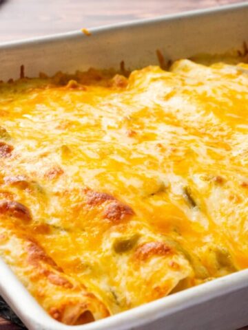An up close look at cheesy sour cream chicken enchiladas in a white baking dish.
