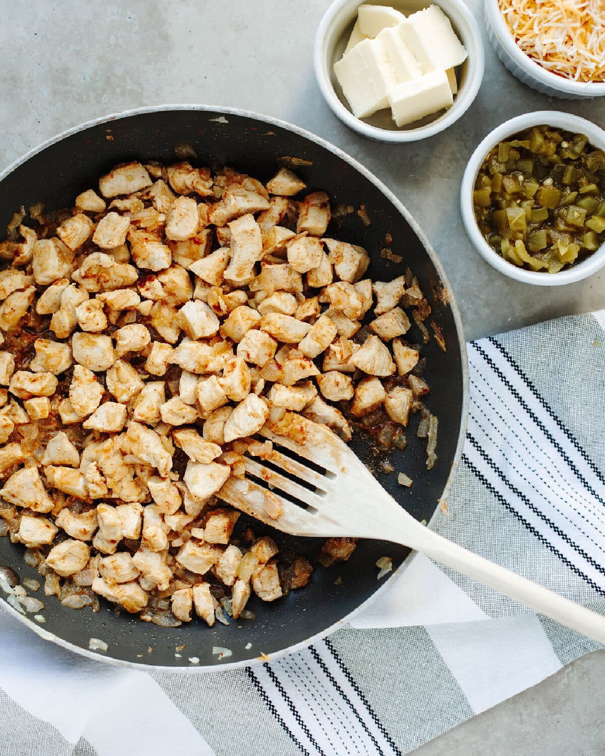 Diced chicken seasoned and cooked in a black skillet with diced onion.