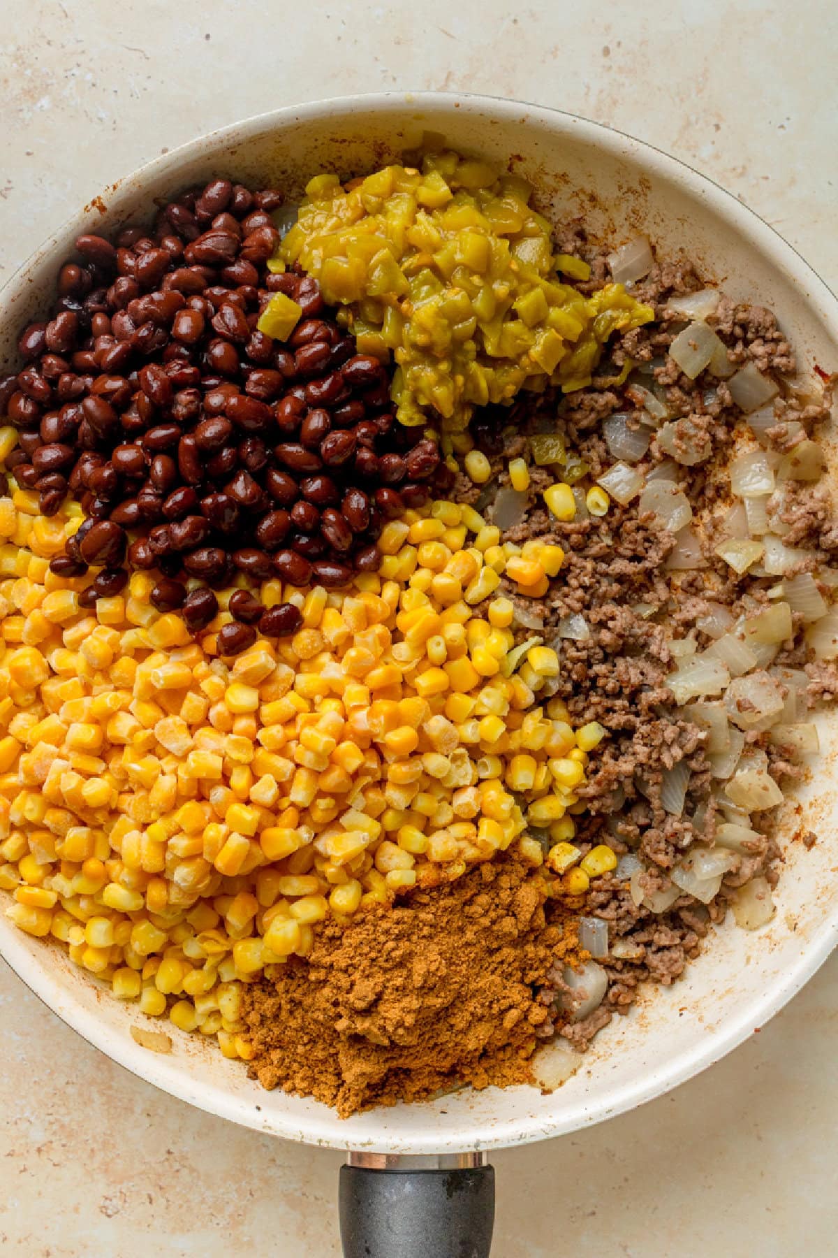 Corn, black beans, green chiles, taco seasoning, ground beef, and onion combined in a skillet.