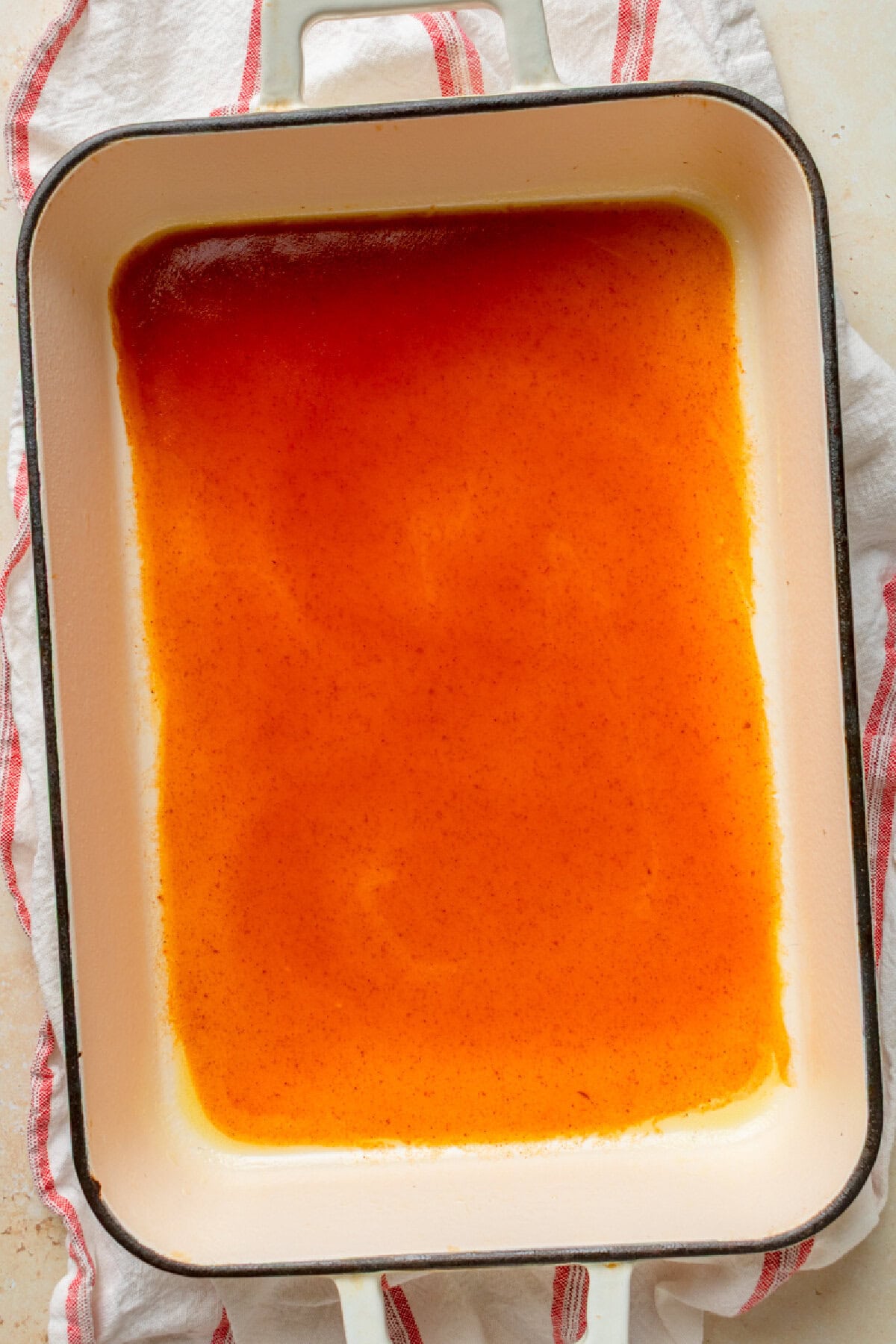 Red enchilada sauce spread in a 9×13 baking dish.
