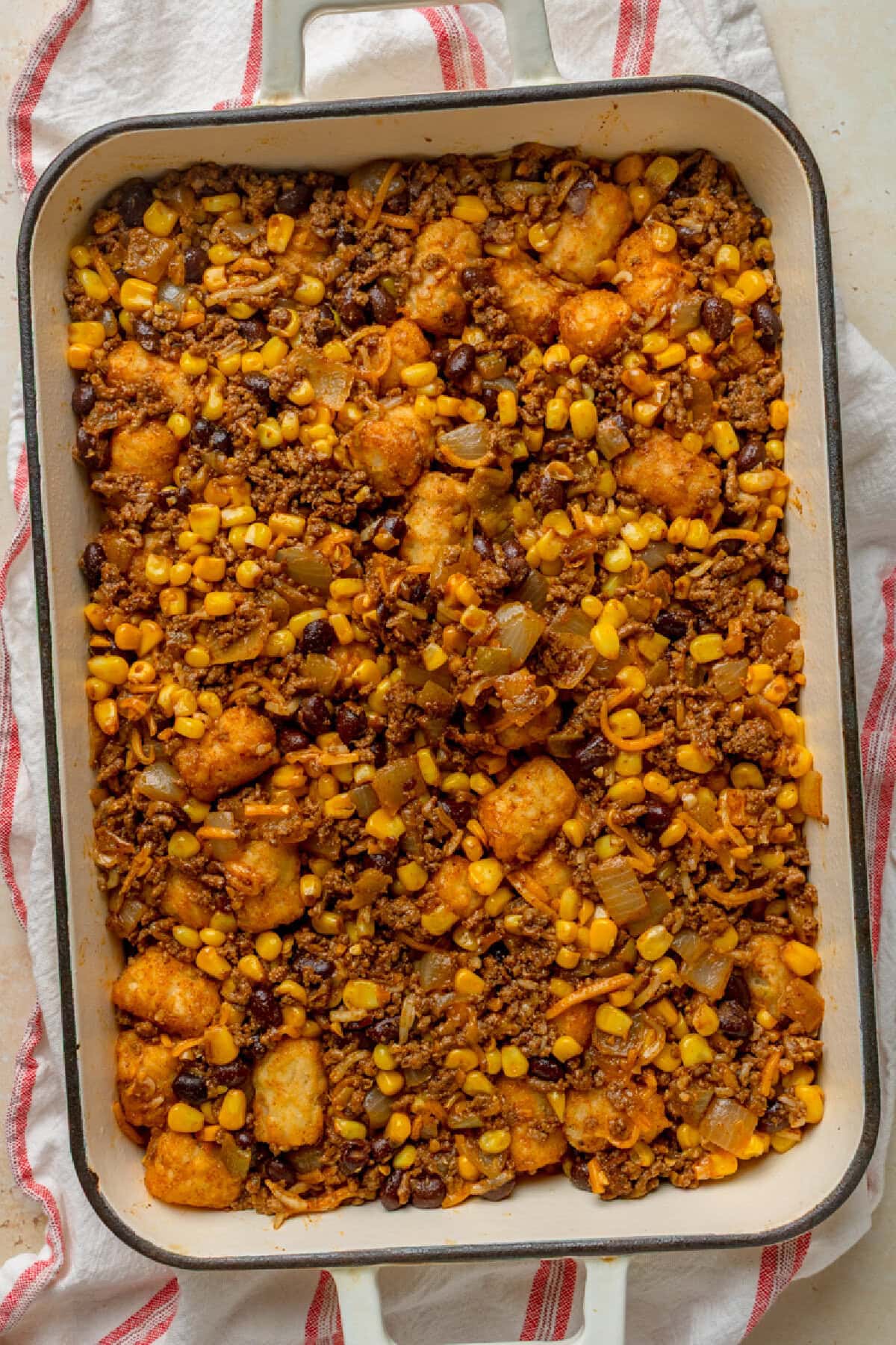 Cooked ground beef, black beans, corn, cheese, and enchilada sauce combined in a baking pan.