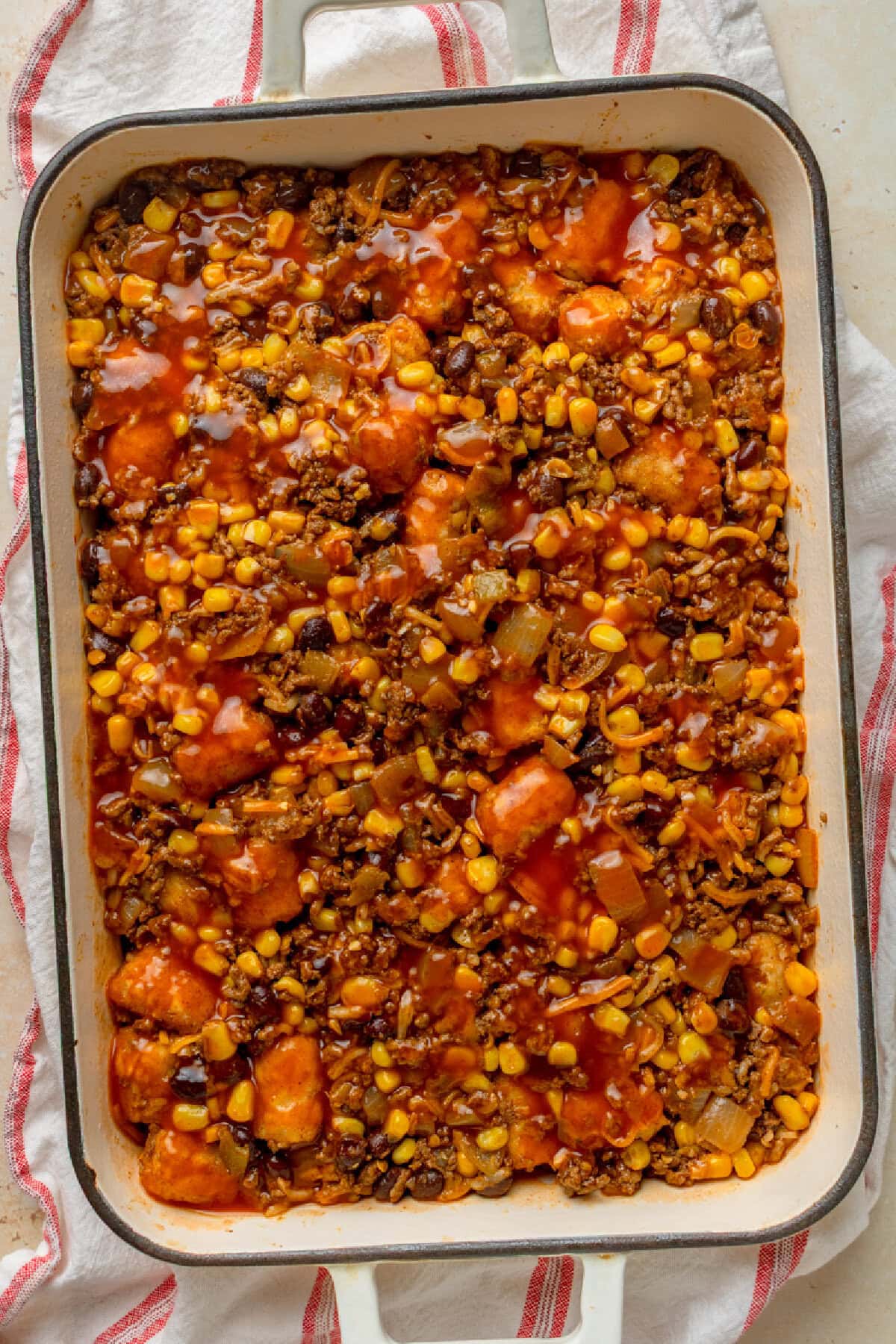 Red enchilada sauce poured on top of tater tot casserole.