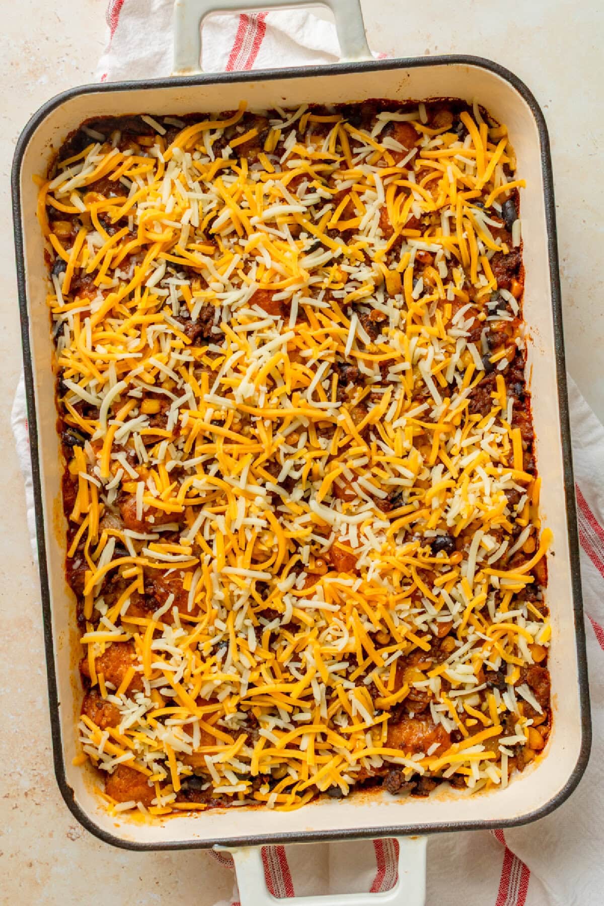 Shredded cheese sprinkled on top of a baked ground beef casserole.