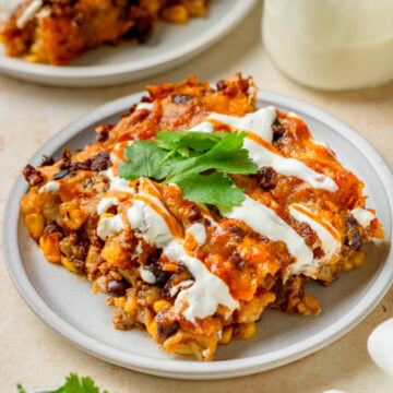 A piece of taco tater tot bake on a plate with sour cream and cilantro.