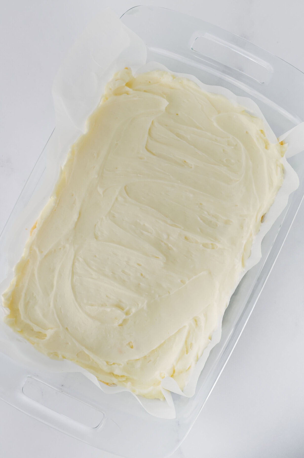 Cream cheese frosting evenly spread on top of a crust in a baking pan.